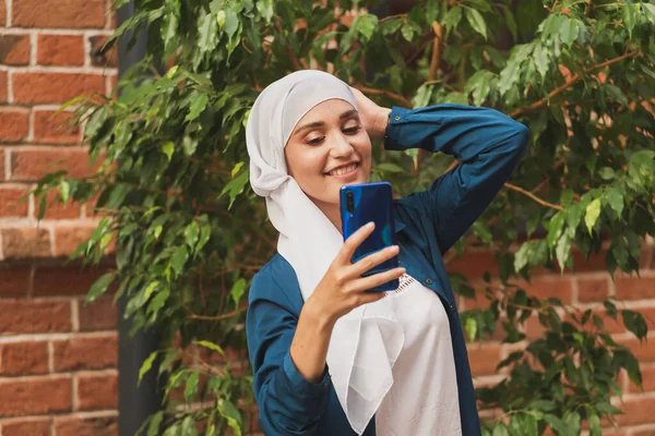 Mulher muçulmana a tirar selfie. Menina bonita feliz com cachecol tirar foto de si mesma usando smartphone. — Fotografia de Stock