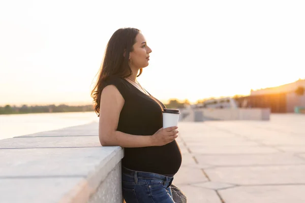 Ung gravid kvinna dricka hämtmat kaffe eller te på vallen. Moderskap, fritid och hälsa koncept. Reklam arbetsplats — Stockfoto