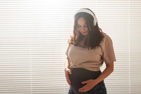 Mulher grávida feliz com cabelo encaracolado ouvir música em fones de ouvido, espaço cópia. — Fotografia de Stock