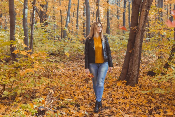 Eine einsame, traurige Frau kickt im Herbst gegen gelbe Blätter. Traurige Stimmung und Konzept der saisonalen affektiven Störung. — Stockfoto