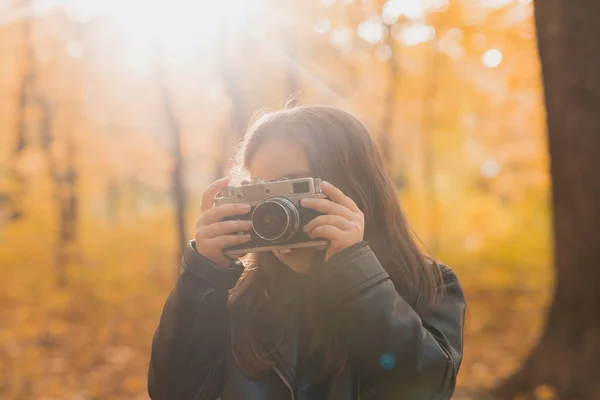 Una niña pequeña tomar una foto con la vieja cámara retro en la naturaleza de otoño. Concepto de ocio y hobby. — Foto de Stock