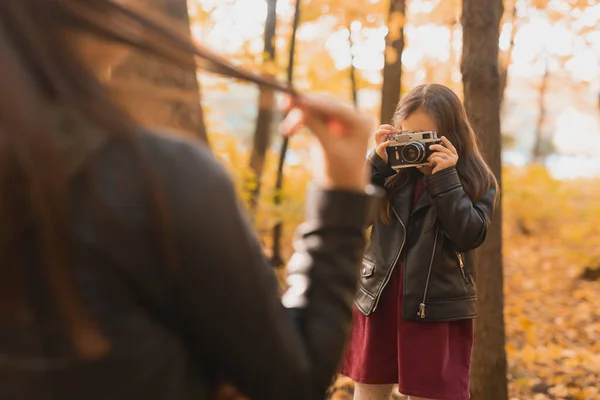 Niña fotógrafa toma fotos de una madre en el parque en otoño. Pasatiempos, arte fotográfico y concepto de ocio. — Foto de Stock