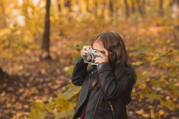 Niña usando una cámara antigua en la naturaleza otoñal. Fotógrafo, temporada de otoño y concepto de ocio. — Foto de Stock