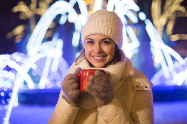 Kış boyunca ayakta duran kız. Arka planda kar yağıyordu. Sıcak ceket şapkası takıyor, çay ve sıcak çay içiyordu..