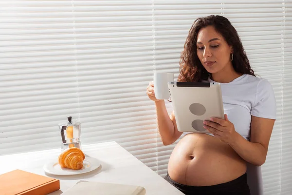 Gravid kvinna som använder digitala tabletter. Dags för frukost. Teknik och graviditet. — Stockfoto