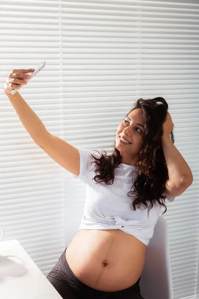Беременная женщина делает автопортрет со своим смартфоном за завтраком — стоковое фото