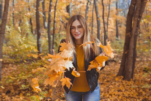 Happy laughing young woman throwing leaves in autumn park. Fall season — Stock Photo, Image