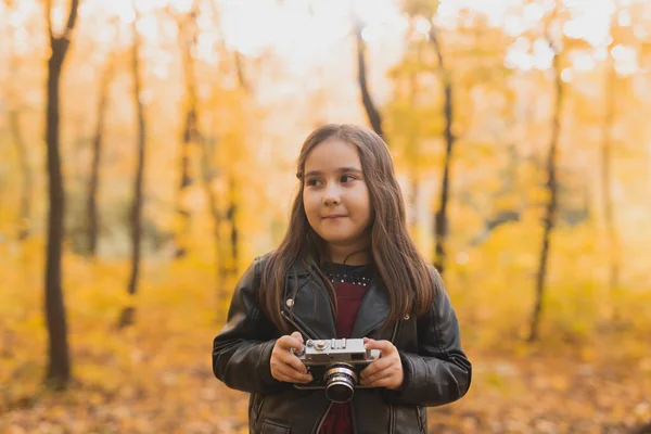 A little girl take a photo with old retro camera in autumn nature. Leisure and hobby concept. — Stock Photo, Image