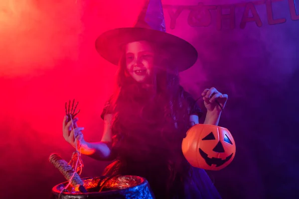 Dziecko dziewczyna czarownica przygotowuje eliksir w kotle w święta Halloween. — Zdjęcie stockowe