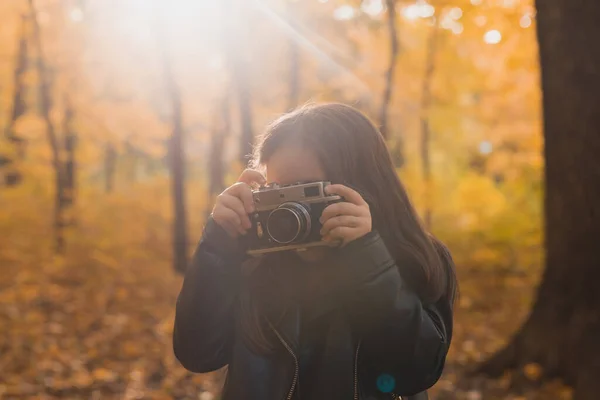 Niña usando una cámara antigua en la naturaleza otoñal. Fotógrafo, temporada de otoño y concepto de ocio. — Foto de Stock