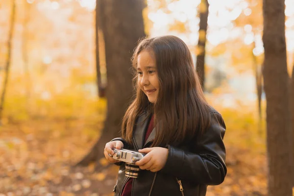 Una niña pequeña tomar una foto con la vieja cámara retro en la naturaleza de otoño. Concepto de ocio y hobby. —  Fotos de Stock