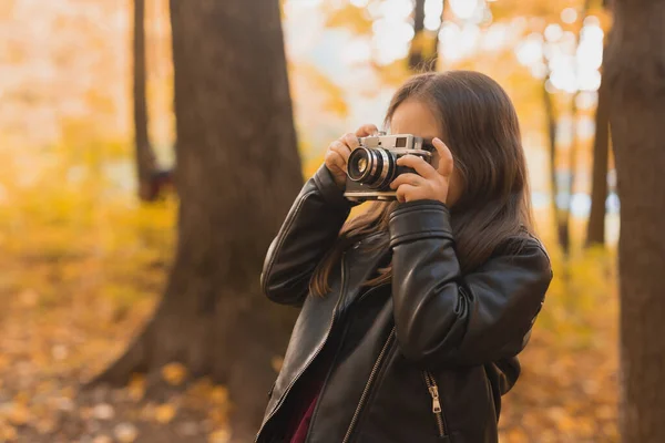 Niña usando una cámara antigua en la naturaleza otoñal. Fotógrafo, temporada de otoño y concepto de ocio. — Foto de Stock