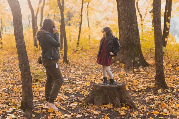 Moeder maakt foto 's van haar charismatische dochter op retro camera in het herfstpark. Hobby 's en vrijetijdsconcept. — Stockfoto