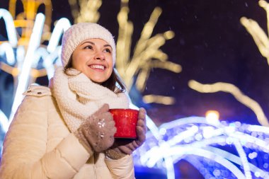 Kış boyunca ayakta duran kız. Arka planda kar yağıyordu. Sıcak ceket şapkası takıyor, çay ve sıcak çay içiyordu..