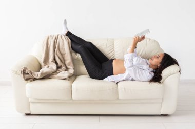 Latin hamile kadın evdeki kanepede yatarken tablet bilgisayar kullanıyor. Ebeveynlik kavramı için hamilelik ve bilgi.