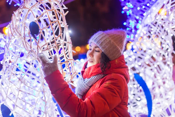 夜の街の照明を背景に冬服を着た幸せな面白い若い女性。クリスマスと冬の休暇のコンセプト. — ストック写真