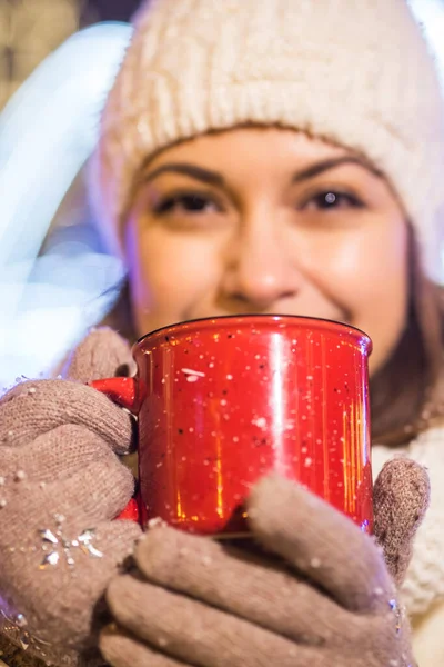 Vacanze di Natale. Bella donna sorridente in abiti caldi con tazza di caffè caldo all'aperto in inverno. Notte di città. — Foto Stock