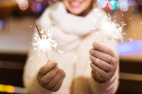 Giovane bella donna in maglia cappello e sciarpa in piedi in città con luce bengala, scintillante. Concetto celebrazione e Natale. — Foto Stock