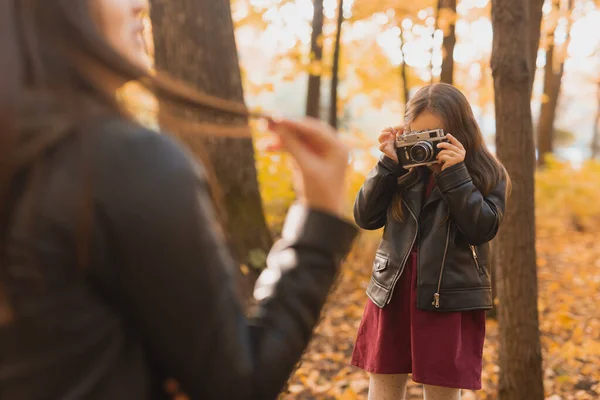 Niño tomando fotos de su madre en cámara retro en el parque de otoño. Hobbies y concepto de ocio. — Foto de Stock