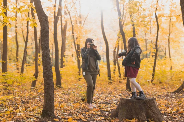 Mãe tirando foto de sua filha carismática na câmera retro no parque de outono. Hobbies e conceito de lazer. — Fotografia de Stock