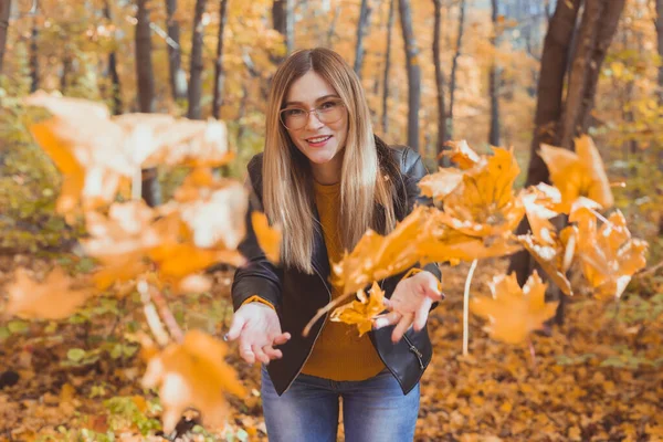 Happy laughing young woman throwing leaves in autumn park. Fall season — Stock Photo, Image
