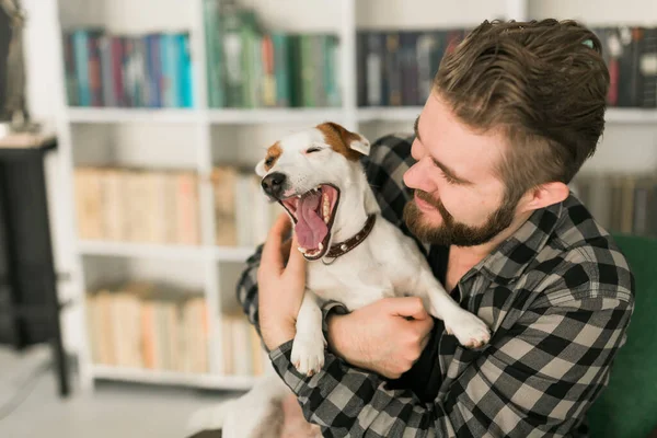 Feliz dueño masculino de gato russell terrier perro, se siente la responsabilidad de cuidar de la mascota, de pie contra los estantes de fondo. Personas y relación con animales — Foto de Stock