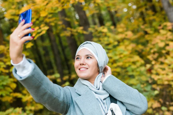 Modische junge muslimische Asiatin im Hidschab, die draußen im Herbstpark ein Selfie mit dem Smartphone macht. Kopierraum. — Stockfoto