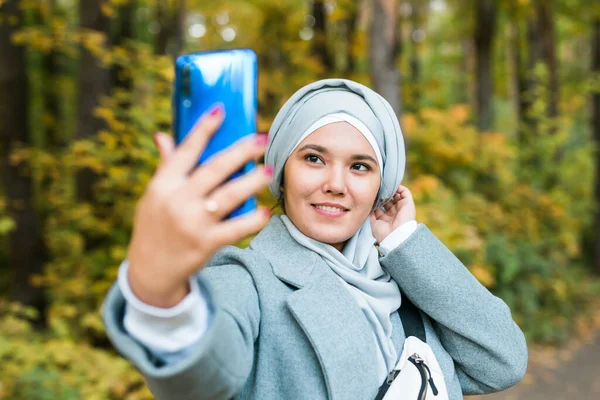 Alla moda giovane musulmana ragazza asiatica in hijab prendendo un selfie su smartphone all'aperto nel parco autunnale. Copyspace. — Foto Stock