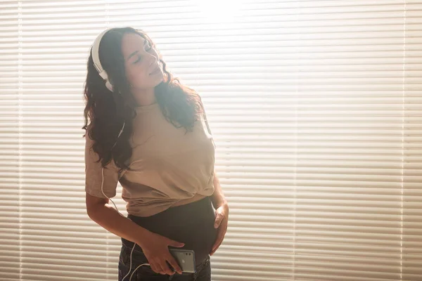 Mujer embarazada escuchar música en los auriculares en casa y bailes, espacio para copiar. — Foto de Stock