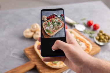 Akıllı telefondan jambonlu ve mantarlı pizza yiyen bir erkek. Sosyal ağlar ve dağıtım gıda uygulaması kavramı.