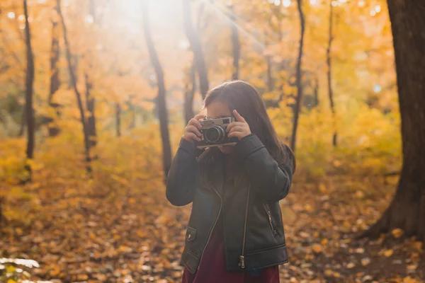 Een klein meisje maakt een foto met oude retro camera in de herfst natuur. Vrijetijdsbesteding en hobby. — Stockfoto