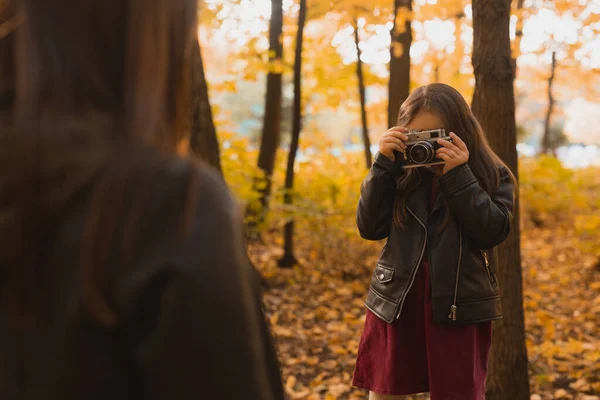 Niño tomando fotos de su madre en cámara retro en el parque de otoño. Hobbies y concepto de ocio. — Foto de Stock