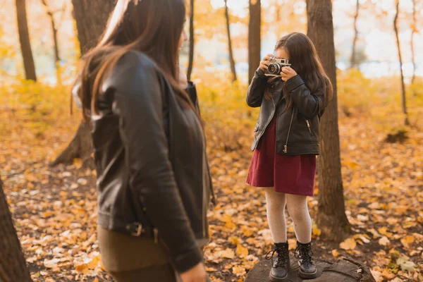 Детская девочка-фотограф фотографирует мать в парке осенью. Хобби, фотоискусство и досуг. — стоковое фото