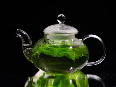 Siyah arka planda sıcak cam çaydanlık, yeşil nane çayı. Bitki çayı ve sağlıklı içecek konsepti.