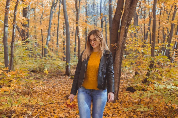 Chica sostiene hojas caídas y camina en el parque de otoño. Concepto estacional. — Foto de Stock