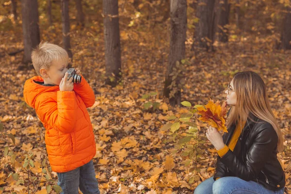 Chłopiec fotograf robi zdjęcia matce w parku jesienią. Zainteresowania, sztuka fotograficzna i koncepcja czasu wolnego. — Zdjęcie stockowe