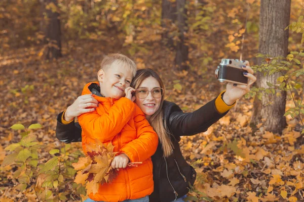 Filho e mãe estão levando selfie na câmera no parque de outono. Conceito de pai solteiro, lazer e outono. — Fotografia de Stock