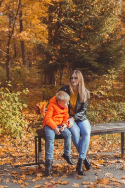 Bekar anne ve çocuk sonbaharda parkta bankta otururlar. Sonbahar sezonu ve aile kavramı.