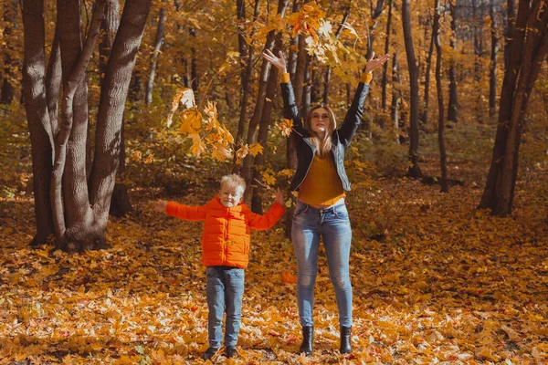 Single parent family playing with autumn leaves in park. Happy mom and son throw autumn leaves up in fall park. — Stock Photo, Image