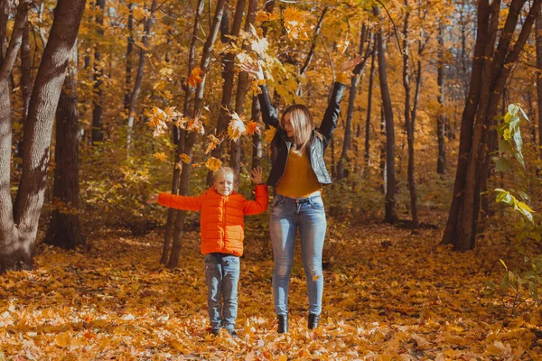 Bekar ebeveynler sonbahar yapraklarıyla parkta oynuyorlar. Mutlu anne ve oğul sonbahar yapraklarını sonbahar parkına atıyorlar.. — Stok fotoğraf