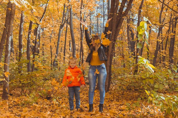 Rodina samoživitelů si hraje s podzimními listy v parku. Šťastná maminka a syn hodit podzimní listí v podzimním parku. — Stock fotografie