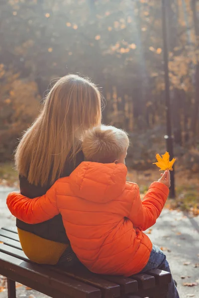 Madre soltera y niño en el otoño en el parque se sientan en el banco. Temporada de otoño y concepto familiar. —  Fotos de Stock