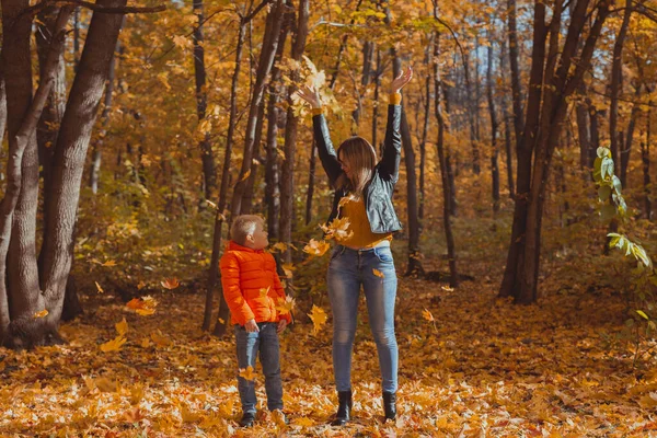 Родители-одиночки играют с осенними листьями в парке. Счастливые мама и сын бросают осенние листья в осенний парк. — стоковое фото