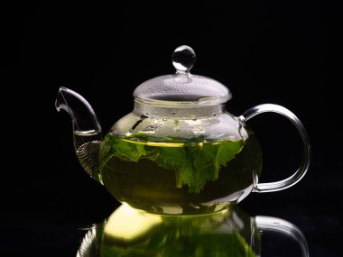 Siyah arka planda sıcak cam çaydanlık, yeşil nane çayı. Bitki çayı ve sağlıklı içecek konsepti.