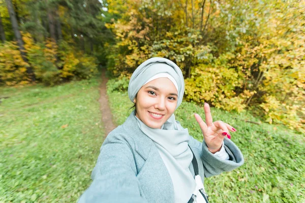 Havalı genç Müslüman Asyalı kız sonbahar parkında açık havada akıllı telefondan selfie çekiyor.. — Stok fotoğraf