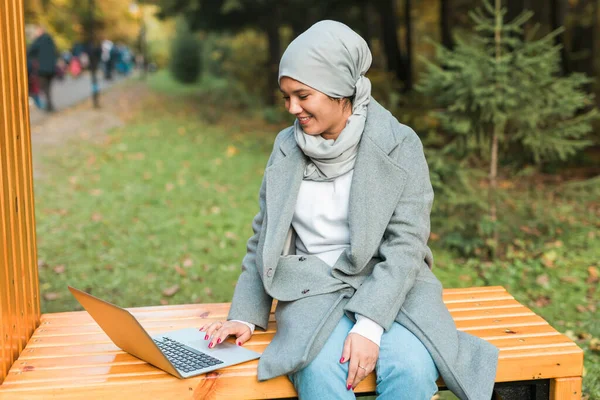 Genç Asyalı Müslüman kadın Autumn Park 'ta dizüstü bilgisayar kullanıyor. Çevrimiçi eğitim, çevrimiçi alışveriş ve sosyal ağlar kavramı. — Stok fotoğraf