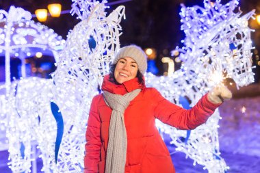 Elinde maytap tutan bir kız. Açık hava kış şehri arka planı, kar, kar taneleri.