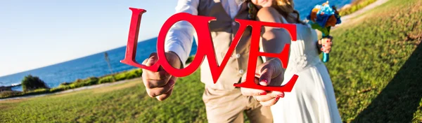 Bride with groom holding bouquet and word love — Stock Photo, Image