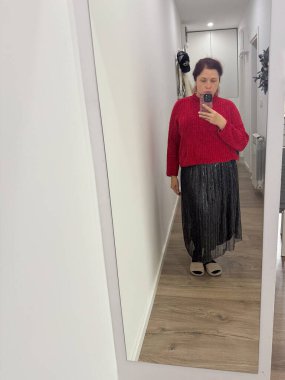 Koridorda kırmızı kazak ve metal etek giyen bir kadın. Gündelik ruh hali, sessiz güven ve modern iç mekanlarda günlük atmosfer.