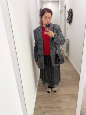 Koridorda poz veren bir kadın. Kırmızı bir kazağın üzerine ekose ceket giymiş. Tarz katmanları, kendini ifade etme ve günlük moda bireyselliği ve şehir yaşam tarzını yansıtıyor.